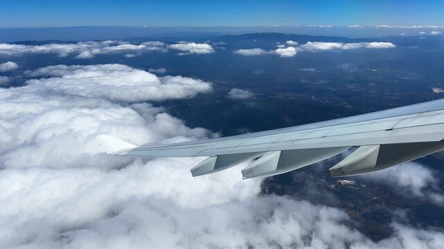 A view of a mountainous landscape through scattered cloud from the window seat of an airplane.