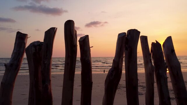 Sunset at Bakhlong Beach near the Thailand&ndash;Cambodia border, framed by rustic wooden posts, with warm sea light and a peaceful tropical shoreline at dusk.