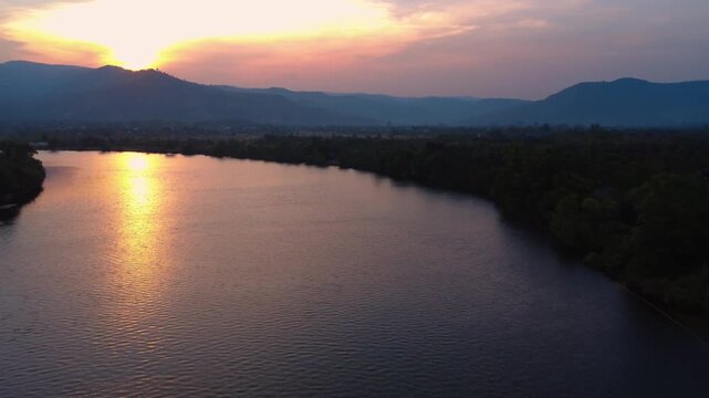 Aerial sunset over a winding river in Kampot Province, Cambodia, with glowing reflections, dark treelines, and distant hills creating a peaceful tropical evening panorama.