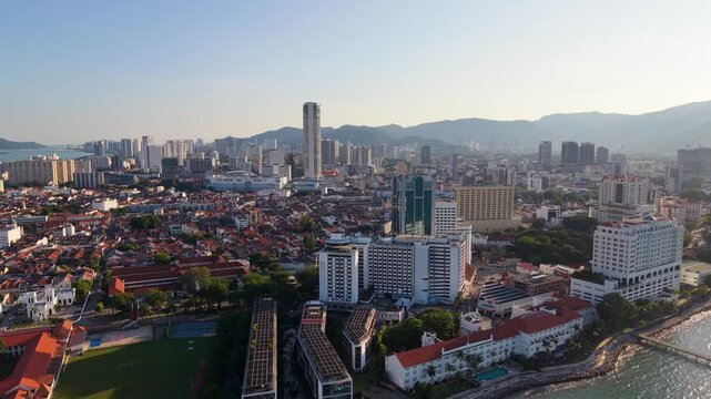 Push away drone shot of Pulau Penang, George Town in Malaysia with mountain range in the background. Sunset view in UHD