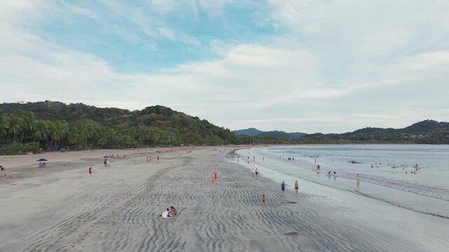 Drone zoom in fast aerial view of wide sandy beach with people walking in Playa Carrillo.