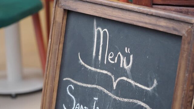 Chalkboard menu sign outside restaurant terrace showcases handwritten specials in sunlight.