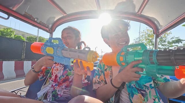 Asian Couple Celebrating Songkran Festival with Water Guns in a Tuk Tuk