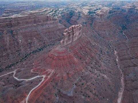 Aerial view of Valley of the Gods featuring a prominent red sandstone butte, winding dirt roads, and layered canyon walls in San Juan County, Utah, United States.