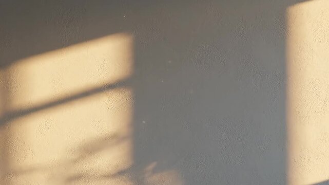 Warm golden hour sunlight casts geometric window shadows across a textured neutral wall creating a peaceful atmosphere