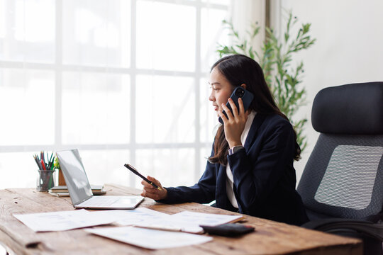 Asian businesswoman multitasking in a modern office with devices