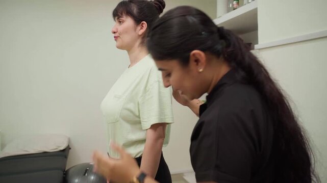 Female physiotherapist performing a posture assessment and correcting a patient's shoulder alignment during a rehabilitation session in a modern medical clinic