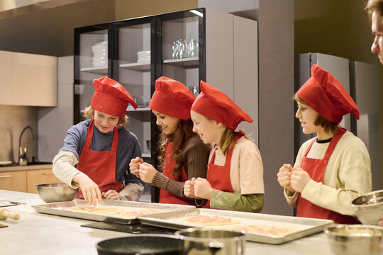 Kids preparing pizza together during cooking class, learning teamwork and food skills in kitchen. Useful for education, culinary workshop, or child development campaigns