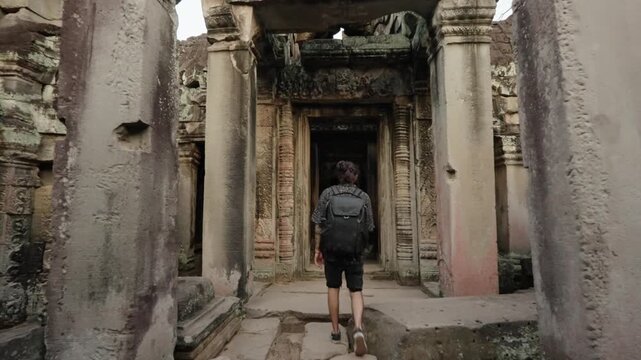 Traveler walking into ancient temple doorway inside Angkor ruins in Cambodia