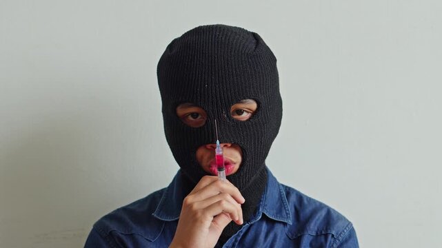 Close up of masked kidnapper or criminal holding medical syringe against white background