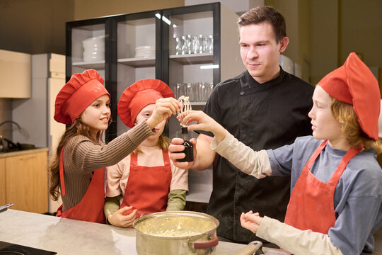 Caucasian male chef guiding children while cooking in kitchen, teaching teamwork and food skills. Useful for culinary class, family learning, healthy eating promotion