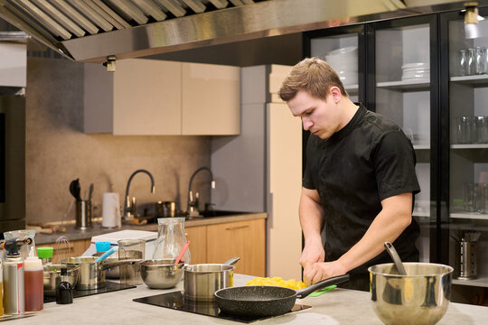 Young adult Caucasian man preparing food in professional kitchen, chopping ingredients for meal production. Ideal for restaurant staffing, culinary training, catering service marketing