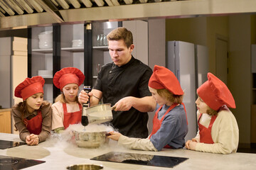 Medium shot of Caucasian male chef teaching children preparing food with liquid nitrogen in cooking...