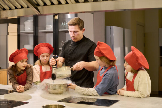 Medium shot of Caucasian male chef teaching children preparing food with liquid nitrogen in cooking class, demonstrating culinary education and teamwork for school or camp promotion