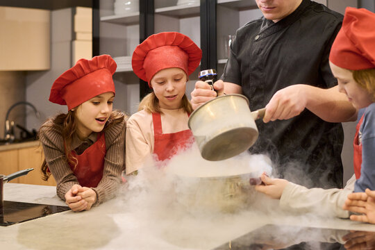 Children watching chef pouring steaming mixture during cooking class in kitchen, learning culinary skills through hands on experiment. Suitable for education, family lifestyle, food workshop promotion