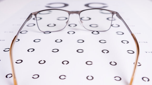 Pair of eyeglasses rests on an eye chart. Brown and silver frames are visible. Concentric circles cover the white background. This is a vision test setup. Ideal for eye care marketing