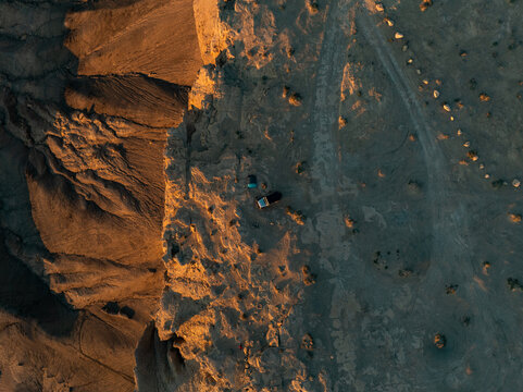 Aerial view of a vehicle and a tent parked near a rugged cliff edge in the desert during golden hour Hanksville, Utah, United States.