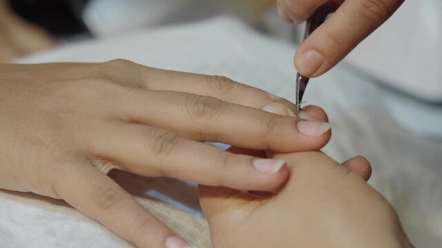Close up of cuticle nipper trimming hangnail during manicure in spa salon.