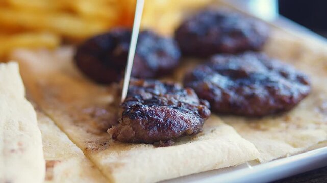 Knife cutting grilled meat patties on flatbread with fork nearby for close up food scene.