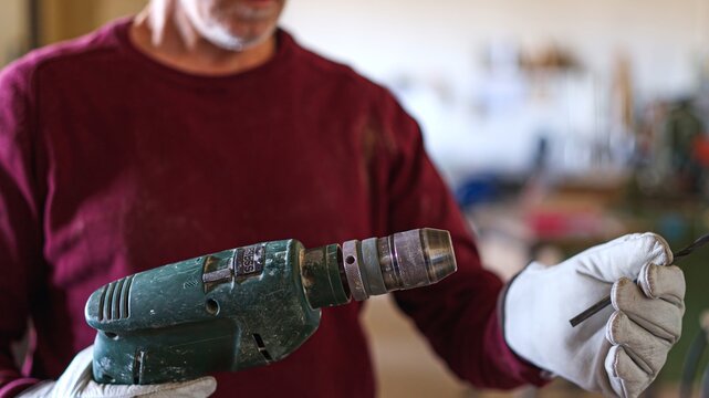 Artisan wearing gloves inserting drill bit into power tool