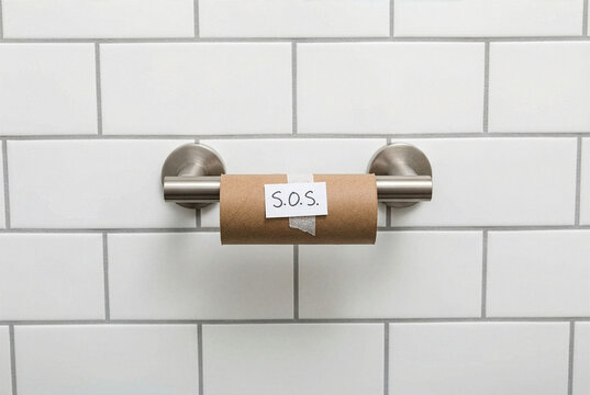 Empty toilet paper roll with an SOS note hanging on a chrome holder in a modern tiled bathroom