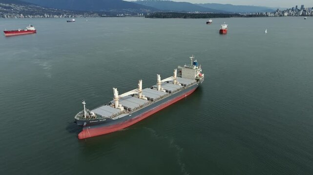 Jericho Beach, Vancouver, British Columbia, Canada - A Massive Cargo Ship Moves Through the Calm Waters, With the Vancouver Skyline in the Background - Orbit Drone Shot