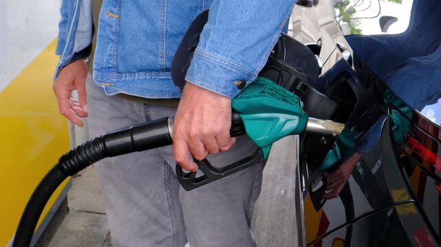 Mid Shot of Unrecognizable Man Hands Pressing Fuel Pump Handle Lever While Refueling Car at Gas Station with Slow Camera Zoom In During Rising Fuel Prices and Cost of Living Increase, Part of a Series