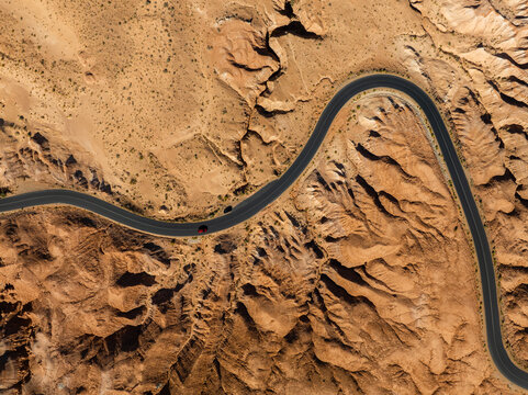 Aerial view of a winding asphalt road through the unique red rock formations of Goblin Valley State Park with a red car in Green River, Utah, United States.