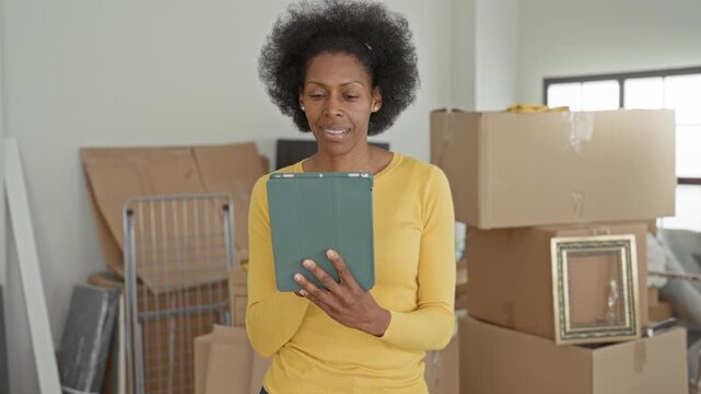 Woman holding tablet with hands visible, smiling amid stacked moving boxes in apartment; moving day joy.