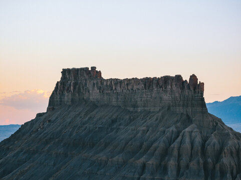 Aerial view of Factory Butte with its distinctive jagged ridges and eroded slopes under a clear twilight sky in Wayne County, Utah, United States.