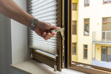 Naklejka premium Close up of hand opening modern window handle in apartment interior with natural light