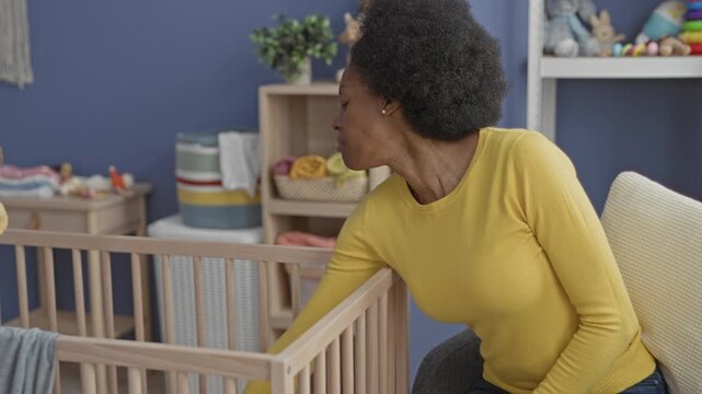 Woman yawning and stretching arms by crib while sitting in a nursery building, reaching toward cradle and rubbing shoulder; exhaustion.