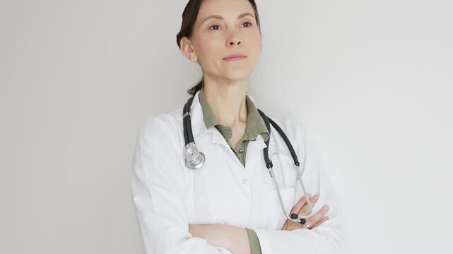 Female medical professional in white lab coat, stethoscope draped, standing with crossed arms and displaying confident, authoritative healthcare demeanor. Medicine and health care