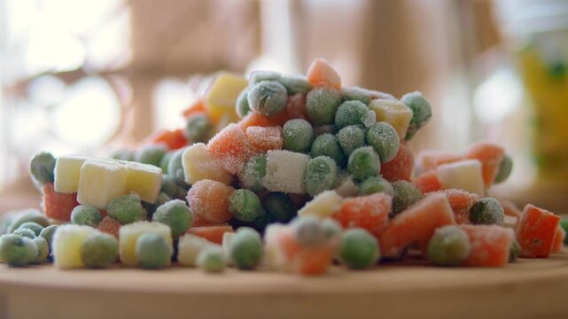 A close up shot of a small pile of frozen mixed vegetables on wooden cutting board.