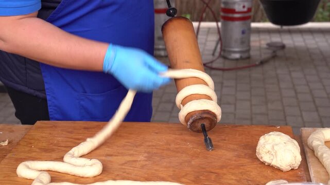 Person wrapping K&uuml;rtőskal&aacute;cs dough on a baking spit for traditional sweet preparation
