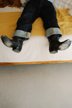 Person on bed with worn cowboy boots on bed in cozy room