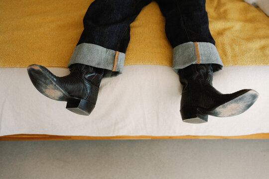 Person on bed with worn cowboy boots on bed in cozy room