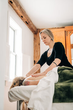 Therapist giving back massage near window in bright spa room
