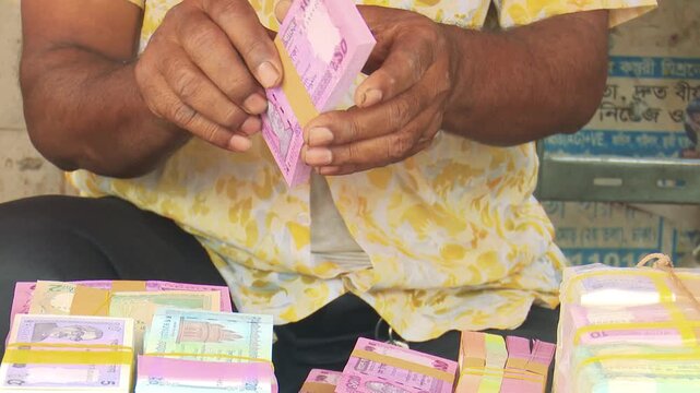 Closeup of hands counting pink currency notes, highlighting financial transactions, budgeting, and everyday money handling in natural indoor setting