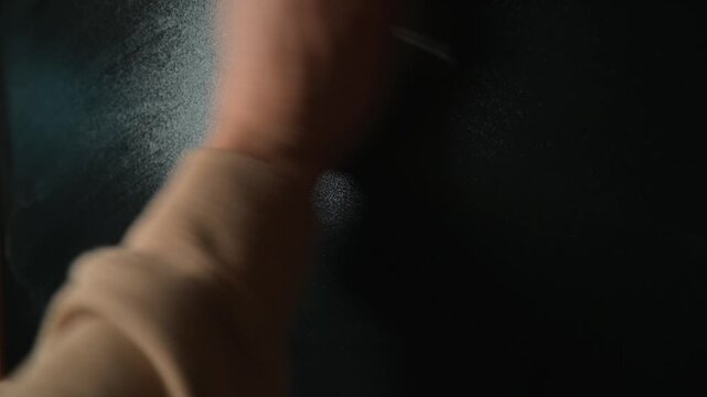 A hand is seen writing mathematical equations on a chalkboard in a classroom. The hand then wipes the chalkboard clean, leaving no trace of the previous writing