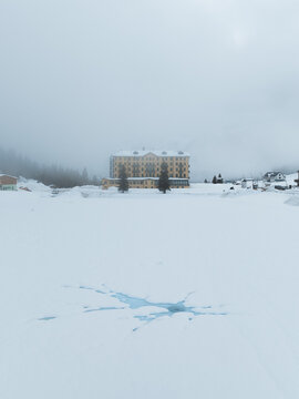 Aerial view of the frozen Lake Misurina with a crack in the ice and the historic Grand Hotel Misurina under a foggy sky in Auronzo di Cadore, Veneto, Italy.