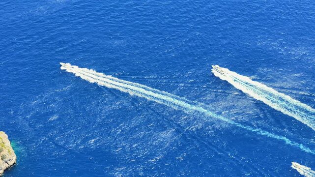 Two boats glide swiftly across the deep blue waters off a picturesque coast during a sunny afternoon