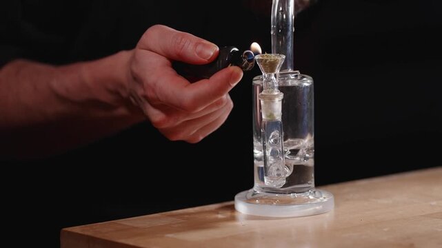 Hand lighting glass water pipe bowl with lighter against dark blue background, water bubbles and boils quickly, walks away after smoking