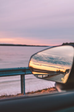 Sunset reflected in car side mirror on a quiet road by the lake