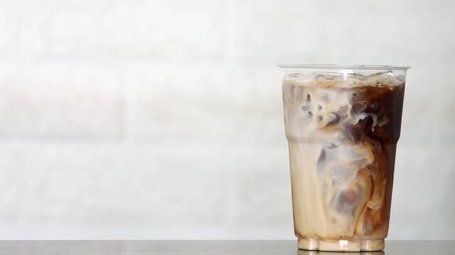 4K Close-up of iced coffee mixed with milk creating beautiful swirl texture Refreshing beverage, Concept ideal for cafe drink menu.