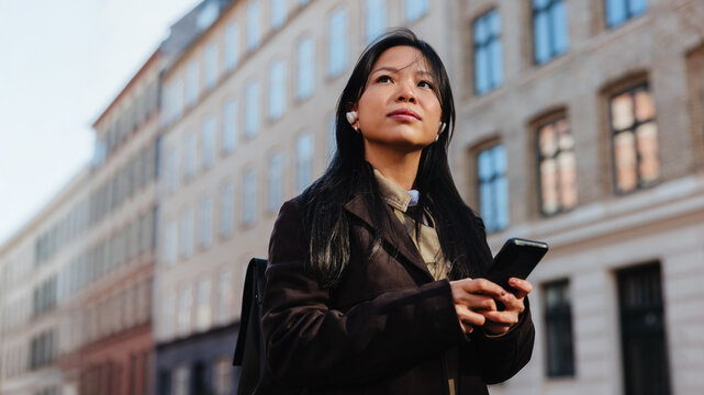 Woman holding phone on a city street looking thoughtful