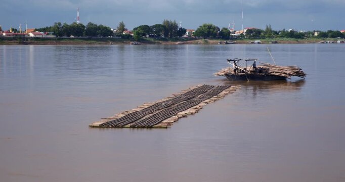 Wooden boat towing the piece of the structure of the new bamboo bridge on the Mekong river near Kampong Cham.