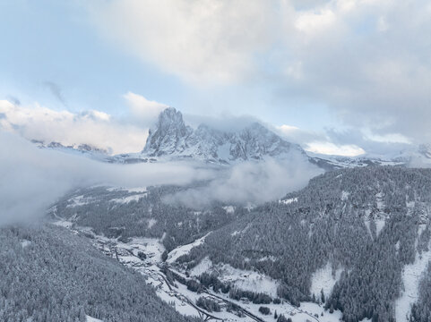 Aerial view of the snow-covered Dolomites mountain range and dense pine forests overlooking the valley in Ortisei, Trentino-Alto Adige, Italy.