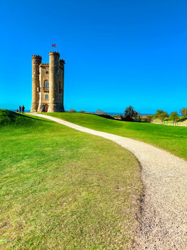 The historic Broadway Tower folly at golden hour with a couple resting on a bench, Cotswolds, UK