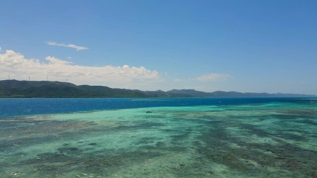 Tropical coral reef teeming with marine life. Anchored boat floating on turquoise waters with coastal mountains in background.